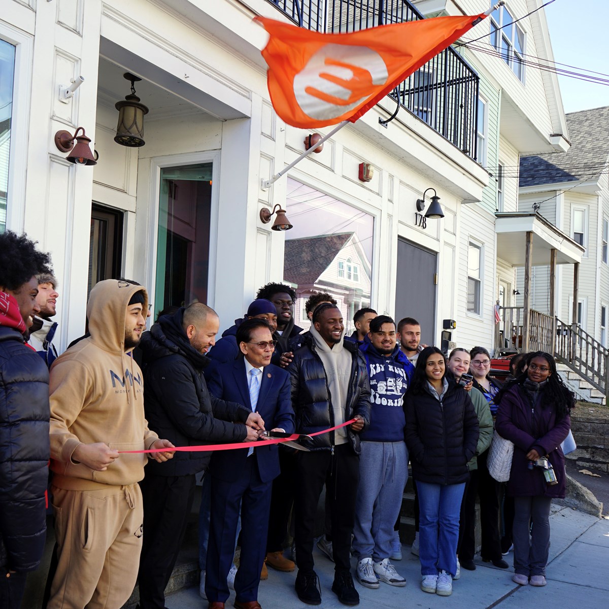 A group of people participate in a ribbon cutting ceremony outside a restaurant.